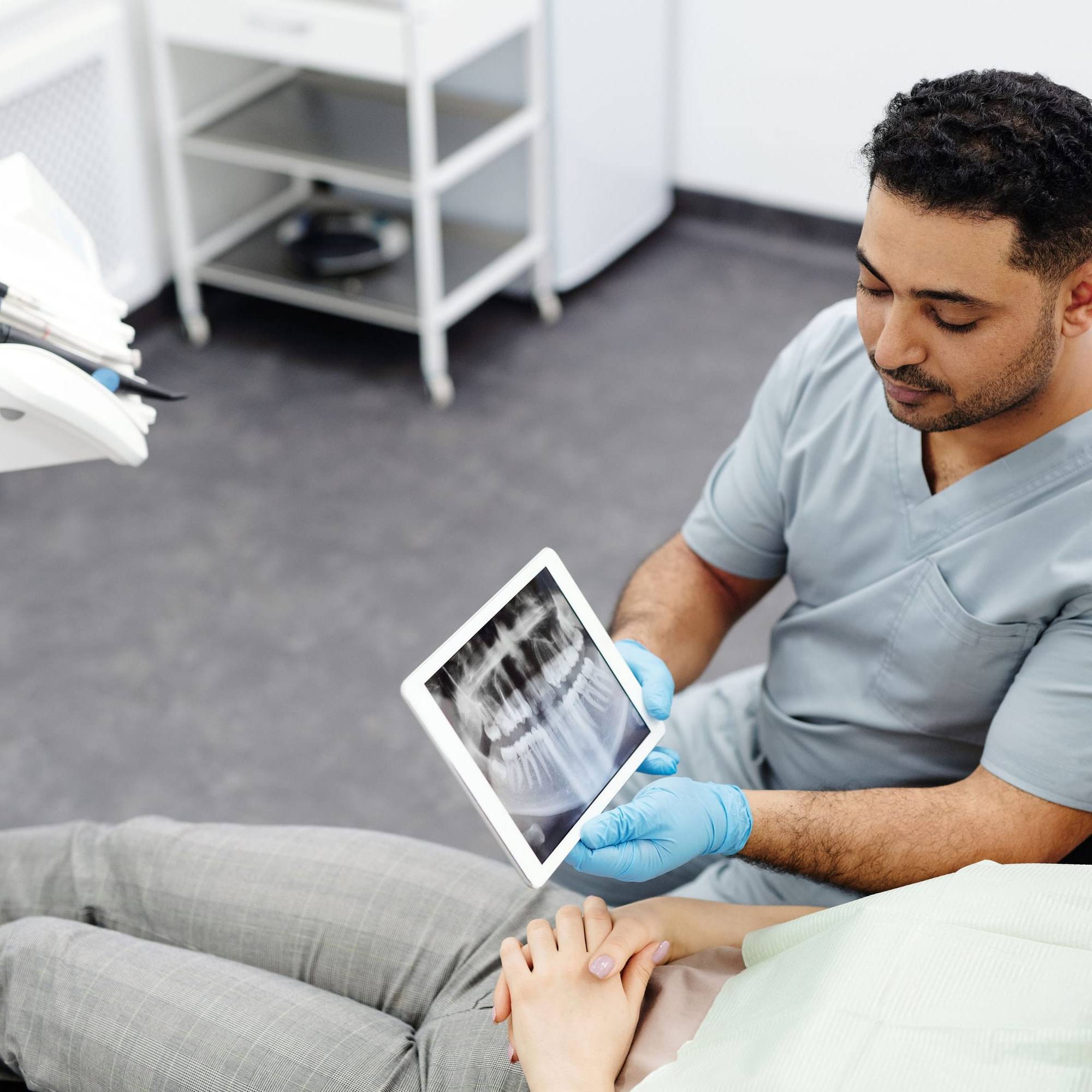 Zahnarzt zeigt einer Patientin im Behandlungsstuhl ihr Röntgenbild auf einem Tablet