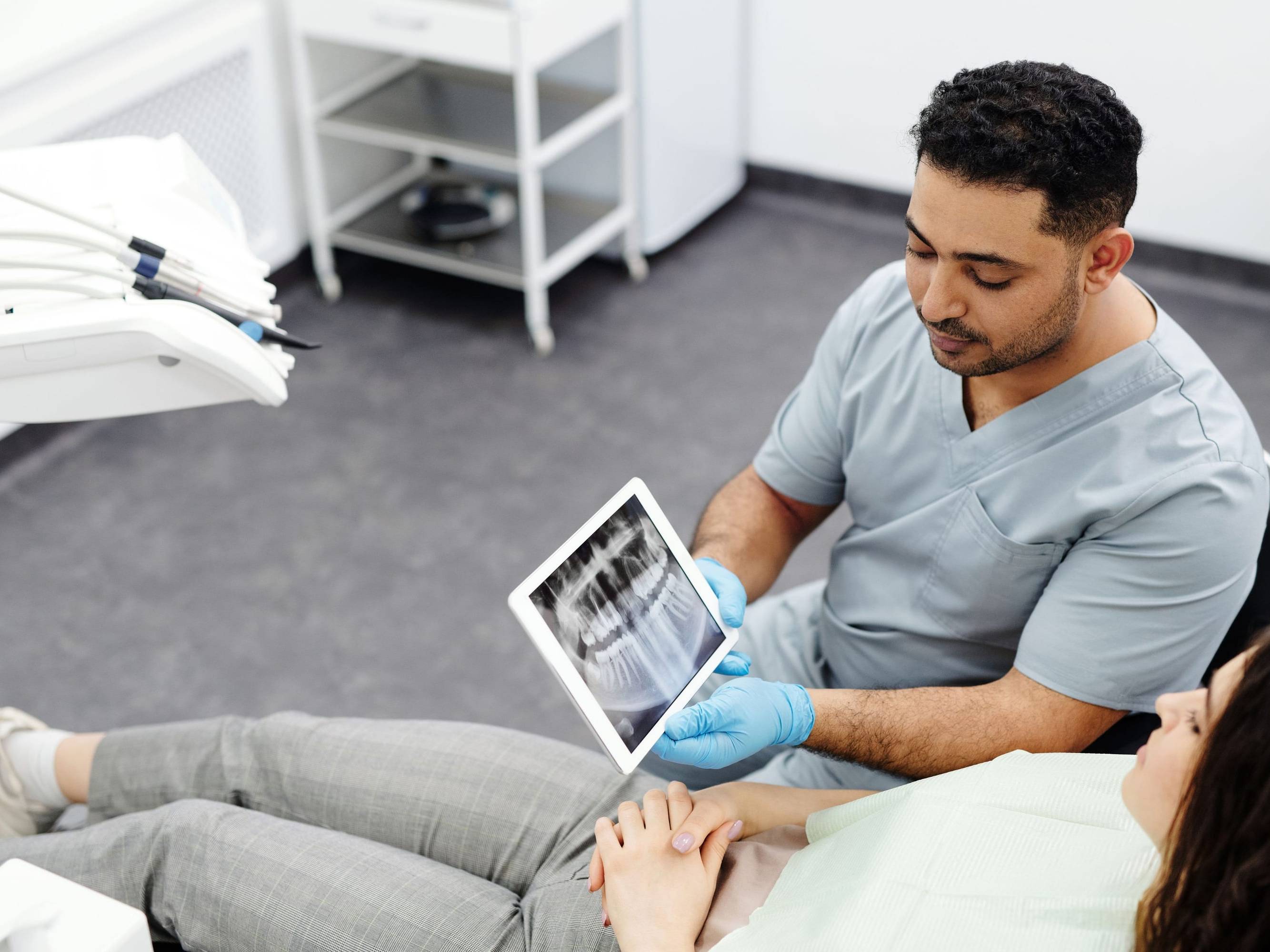 Zahnarzt zeigt einer Patientin im Behandlungsstuhl ihr Röntgenbild auf einem Tablet