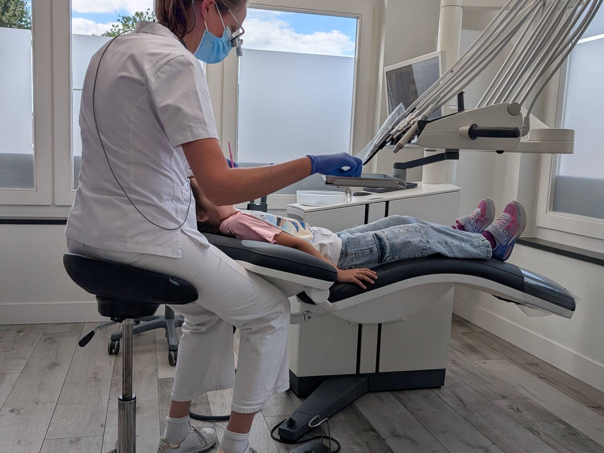 Zahnärztin untersucht ein Kind im Behandlungsstuhl in einem hellen Raum